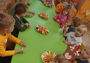 Dzieci siedzą przy stoliku i jedzą poczęstunek od Jagody