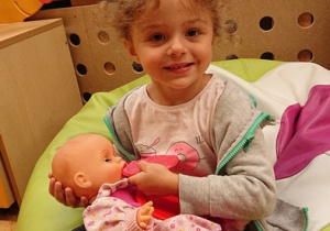 Dziewczynka siedzi na pufie i karmi lalkę