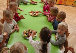 Dzieci siedzą przy stole i zjadają poczęstunek od Kubusia