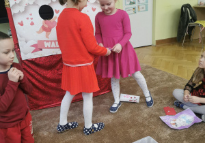 dzieci wręczają sobie kartki walentynkowe, siedzą na dywanie, ubrane w czerwone ubrania 6