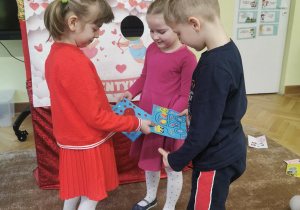 dzieci wręczają sobie kartki walentynkowe, siedzą na dywanie, ubrane w czerwone ubrania 11