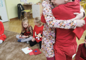 dzieci wręczają sobie kartki walentynkowe, siedzą na dywanie, ubrane w czerwone ubrania 17