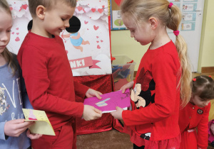dzieci wręczają sobie kartki walentynkowe, siedzą na dywanie, ubrane w czerwone ubrania 18