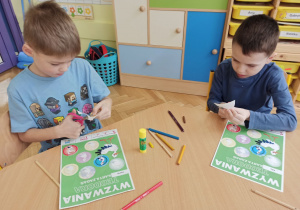 dwaj chłopcy siedzą przy stole i wycinają odznakę