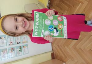 uśmiechnięta dziewczynka pokazuje kartkę, na której nakleiła odznakę