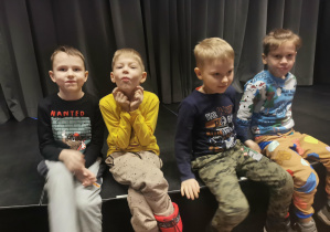 czterech uśmiechniętych chłpców dzieci na scenie teatru, w tle kurtyna