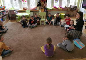 Dzieci siedzą w kole na dywanie, śród nich pani logopeda