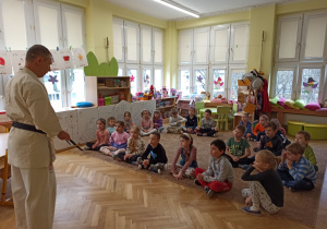 trener opowiada o pasie w karate dzieci siedxzą na dywanie i słuchają