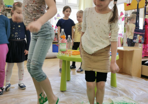 dwie dziewczynki skaczą po tkaninie, na stopach mają zieloną farbę