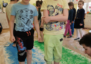 dwaj chłopcy stoją na tkaninie, uśmiechają się do zdjęcia, ich stopy są w niebieskiej farbie