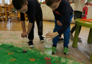dwoje dzieci robią stemple w kształcie kwiatków używając plastikowych butelek