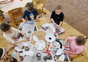 kilkoro dzieci siędzi przy stole i konstruuje bociana z papierowych talerzyków, zdjęcie z góry