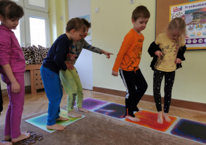 dzieci chodzą po planszach sensorycznych ułożonym na dywanie w sali