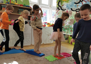 dzieci chodzą po puzzlach sensorycznych ułożonym na dywanie w sali