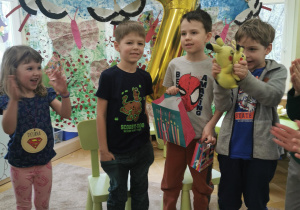 dwaj jubilaci stoją na dywanie, między nimi złoty balon z helem przedstawiający cyfrę 7