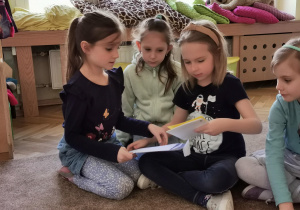 trzy dziewczynki otwierają kopertę z zadaniem