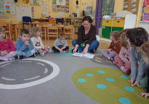 Dzieci siedzą na dywanie i słuchają opowiadania