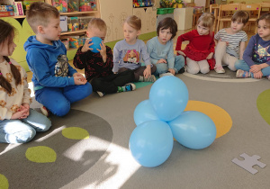 Dzieci siedzą w kole i podają sobie balonik