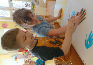 Dzieci odbijają dłoń pomalowaną farbą na szablonie motylka