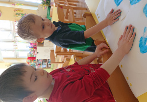 Dzieci odbijają dłoń pomalowaną farbą na szablonie motylka