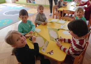 Dzieci siedzą przy stole i wypychają szablon baranka