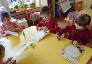 Dzieci siedzą przy stole i wypychają szablon baranka