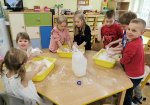 dzieci wyrabiają białą masą plastyczną w żółtych pojemnikach