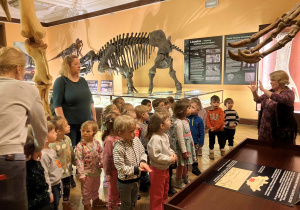 Dzieci słuchają opowiadania przewodnika w muzeum na temat życia dinozaurów