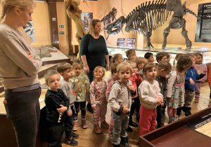 Dzieci słuchają opowiadania przewodnika w muzeum na temat życia dinozaurów