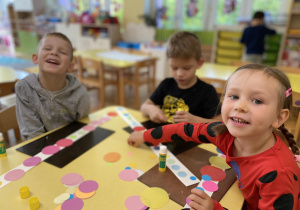 Dzieci siedzą przy stole i przyklejają kolorowe koła do paska