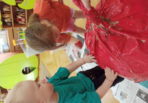 Dzieci malują wielkie jabłko z papieru czerwoną farbą za pomocą dłoni.