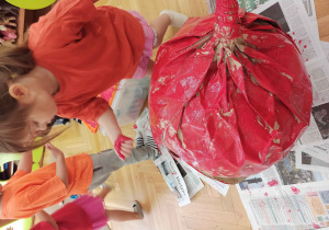 Dzieci malują wielkie jabłko z papieru czerwoną farbą za pomocą dłoni.