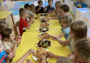 Dzieci siedzą przy stole i jedzą poczęstunek od jubilata