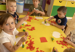 Dzieci siedzą przy stole i wyklejają szablon jabłka