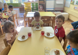 Dzieci siedzą przy stole i jedzą ciasto