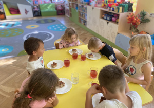 Dzieci siedzą przy stole i jedzą ciasto
