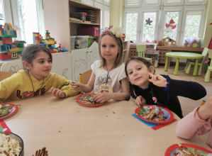 trzy uśmiechnięte dziewczynki siedzą przy stole, jedzą ciasto