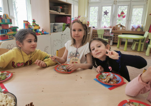 trzy dziewczynki uśmiechają się siedząc przy stole i jedząc ciasto urodzinowe