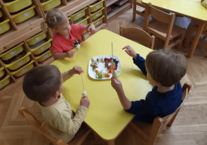 Dzieci nadziewają owoce na patyczki do szaszłyków.