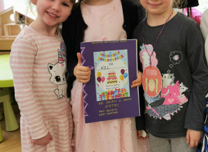 trzy dziewczynki uśmiechają się, jubilatka trzyma album urodzinowy