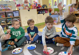 dzieci siedzą na dywanie i pokazują swoje emocje wykonane na talerzu