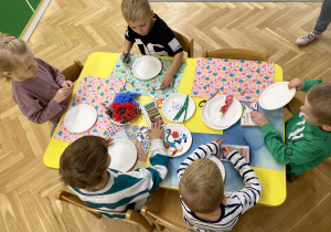 dzieci siedzą przy stole i wykonują pacę