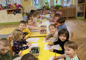 dzieci siedzą przy stoliku i kolorują dla jubilatki