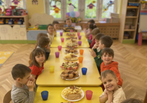 dzieci siedzą wokół wspólnego stołu przy poczęstunku