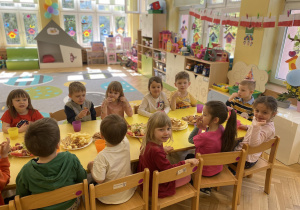 dzieci siedzą wokół wspólnego stołu przy poczęstunku