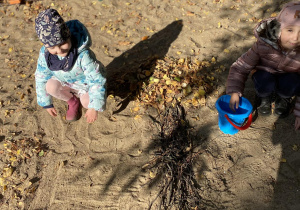 dzieci układają drzewo z patyczków, kasztanów i liści