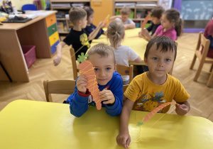 dzieci siedzą przy stole i ozdabiają włóczką szablon marchewki