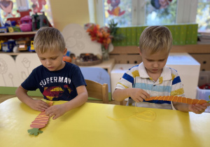 dzieci siedzą przy stole i ozdabiają włóczką szablon marchewki