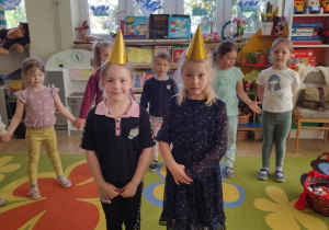 dwie dziewczynki w urodzinowych czapkach stoją w środku koła
