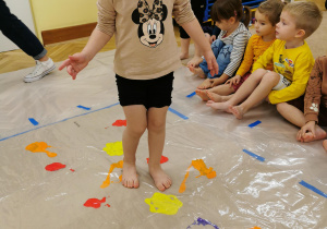 dzieci rozprowadzają farbę stopami po dużym kartonie